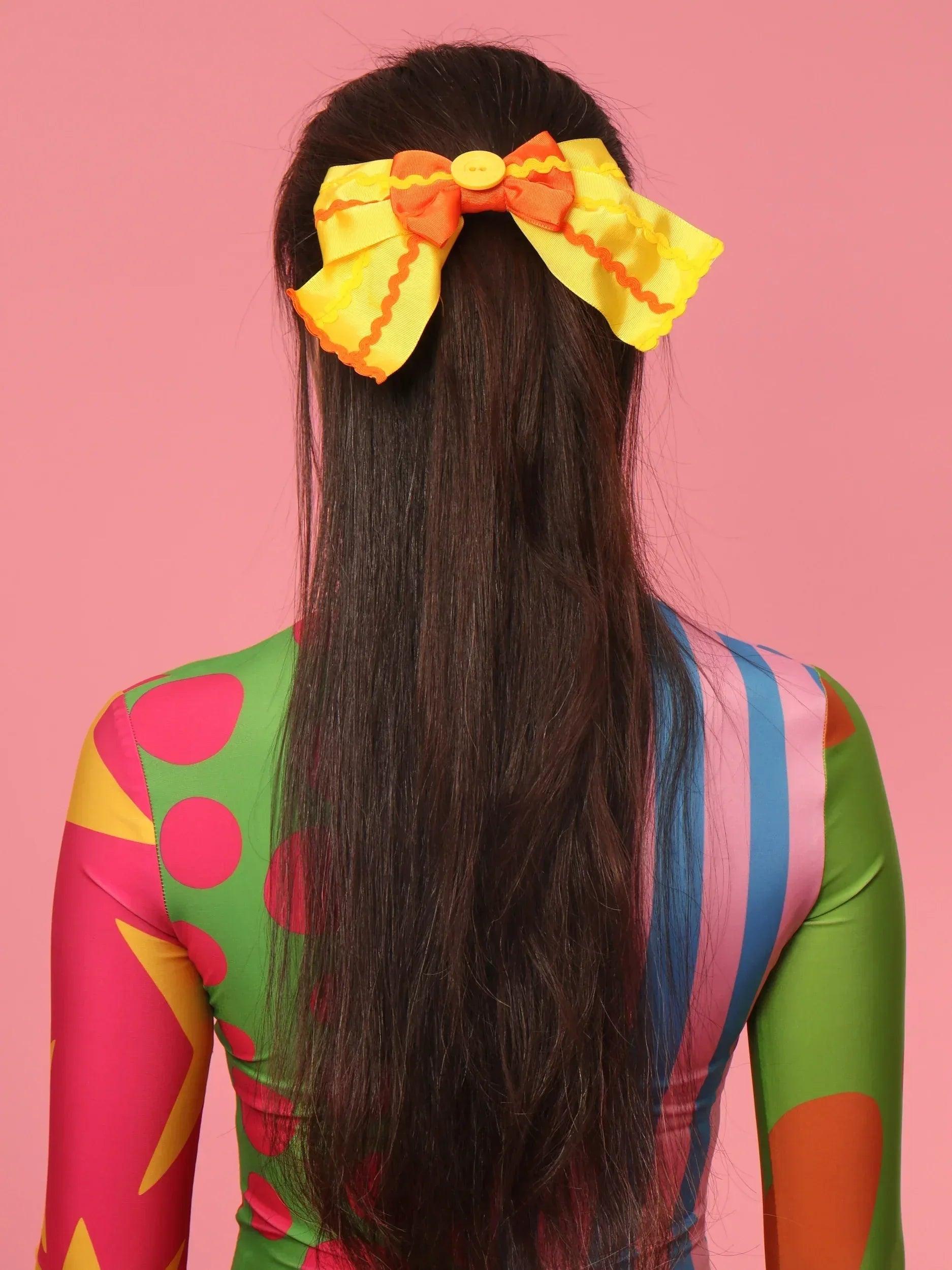 Pasador Cosima con moño amarillo y naranja sujeto al cabello