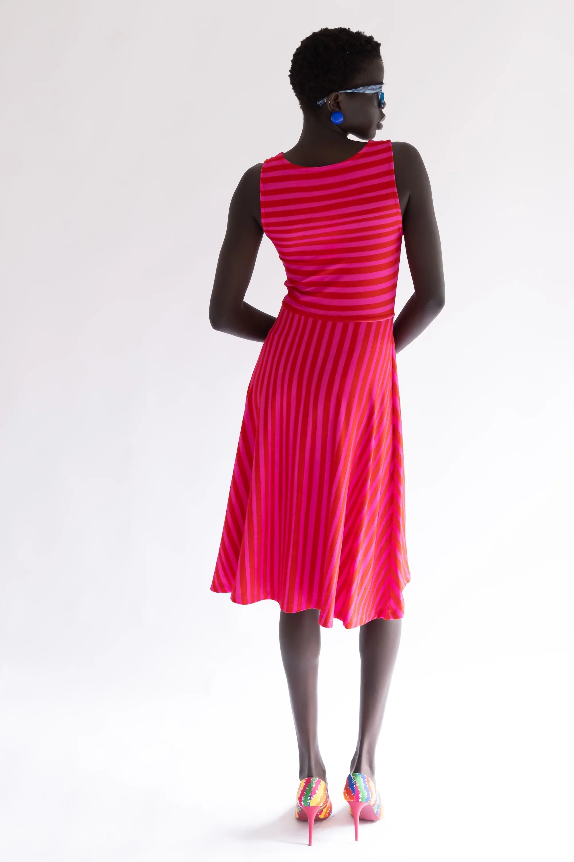 Vestido sin mangas de rayas fucsia y rojo, escote V y falda plisada.