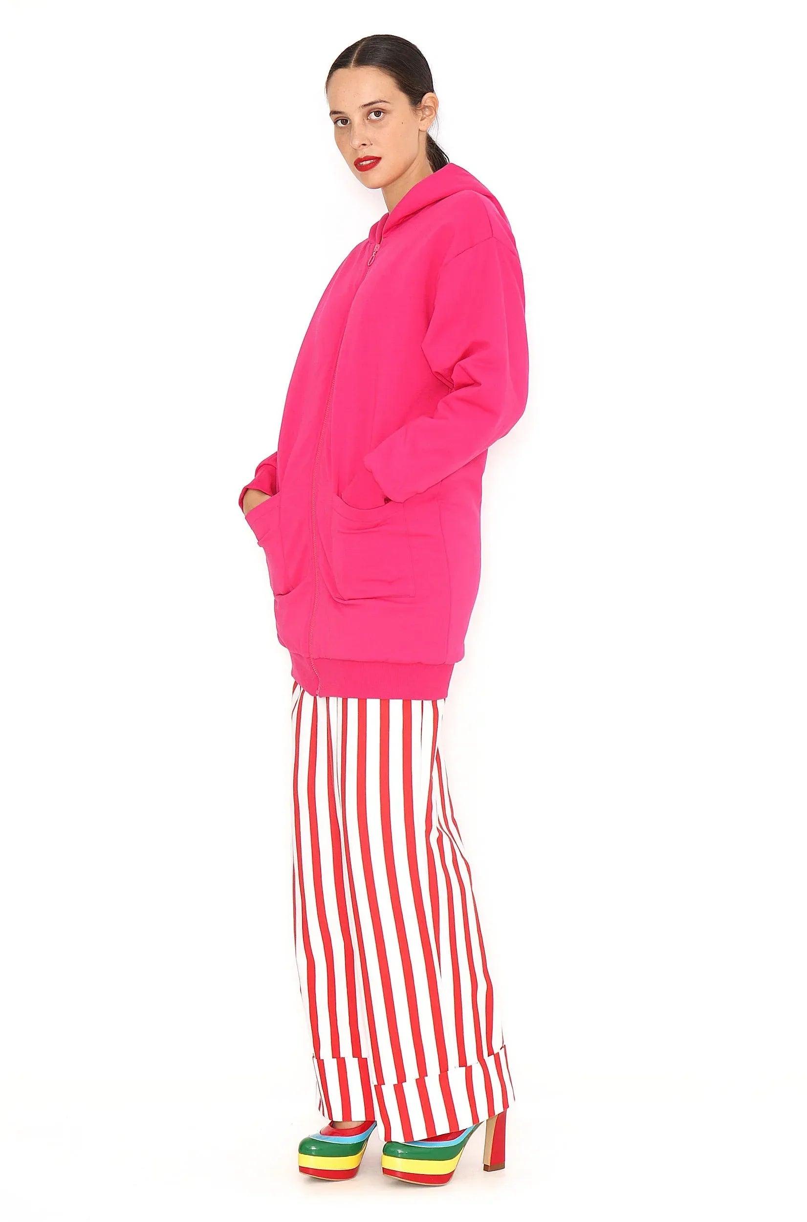 Chaqueta larga fucsia con capucha y bolsillos laterales, cierre frontal visible.