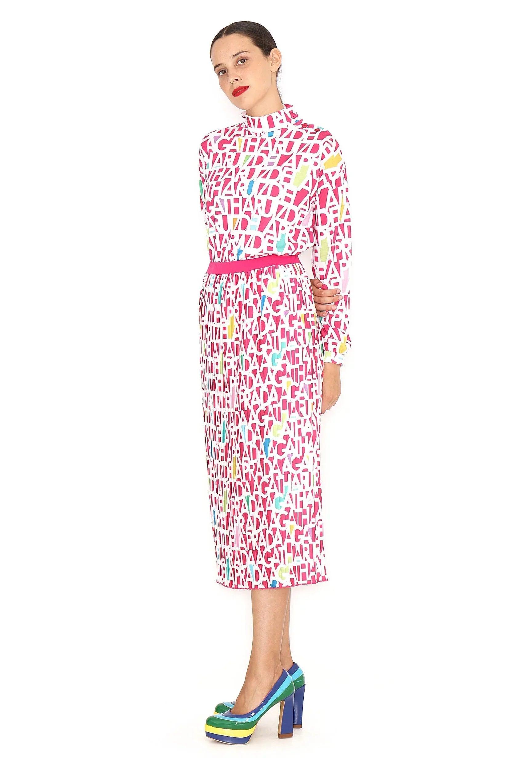 Falda midi plisada estampada con letras, rosa y verde, sobre fondo blanco.