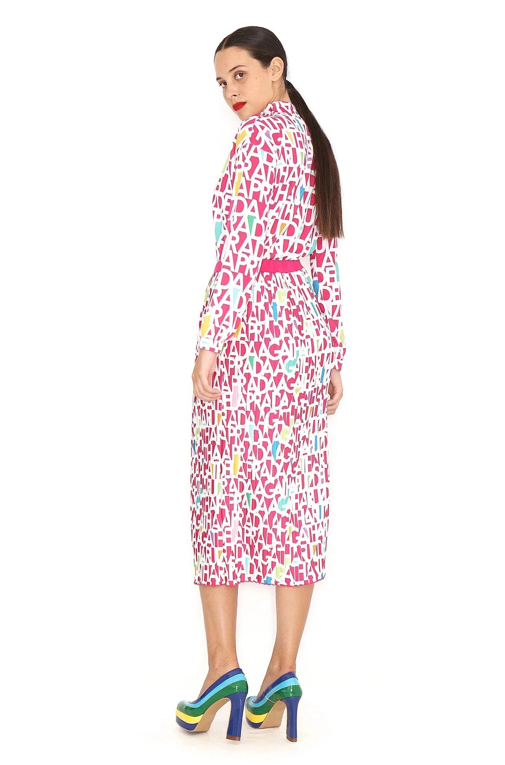 Falda midi plisada con estampado de letras rosa y blanco, caída recta a media pierna.