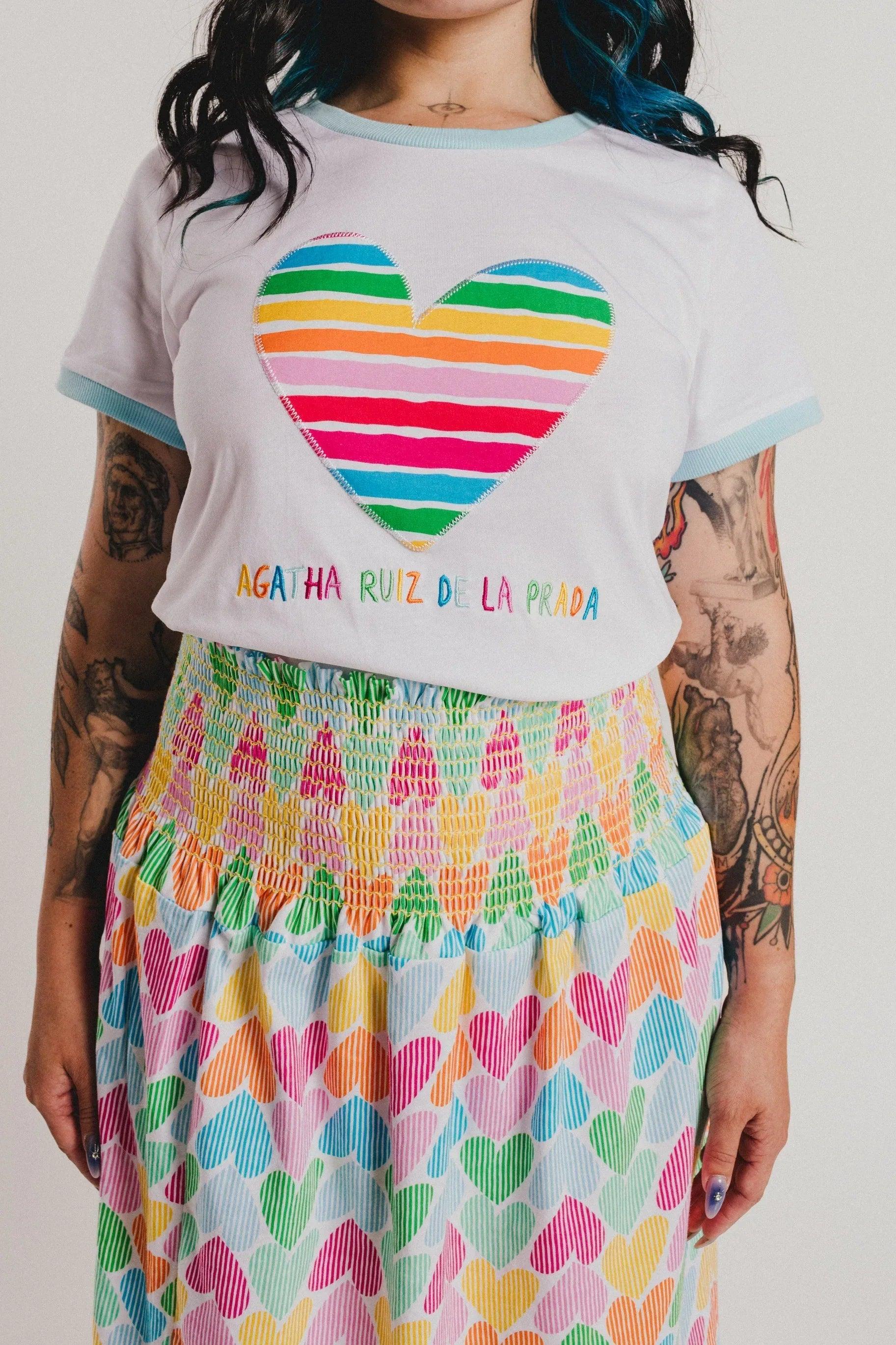 Camiseta blanca con corazón arcoíris a rayas, texto multicolor y cuello azul