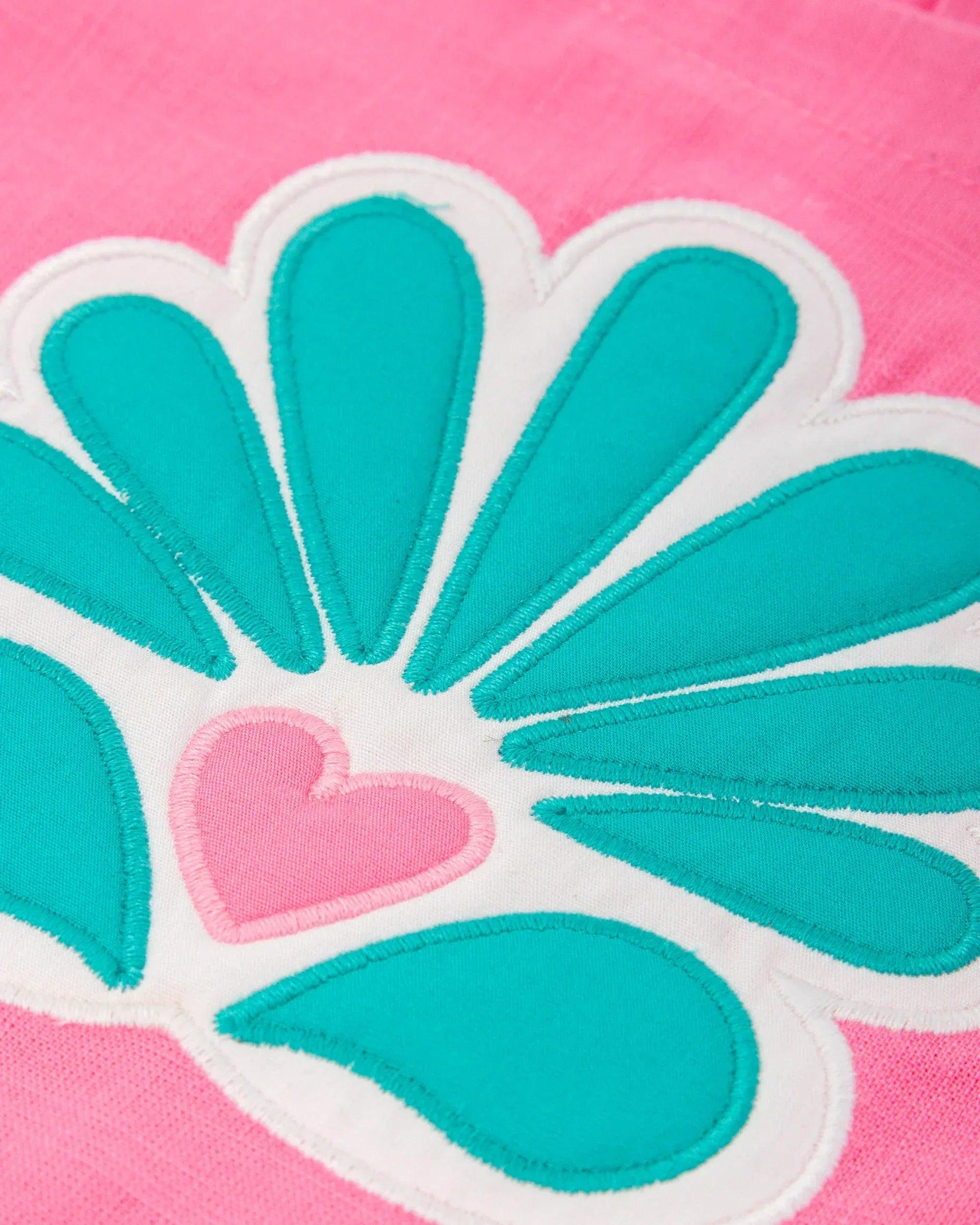 Detalle de flor turquesa y rosa en vestido de algodón fucsia, con borde blanco