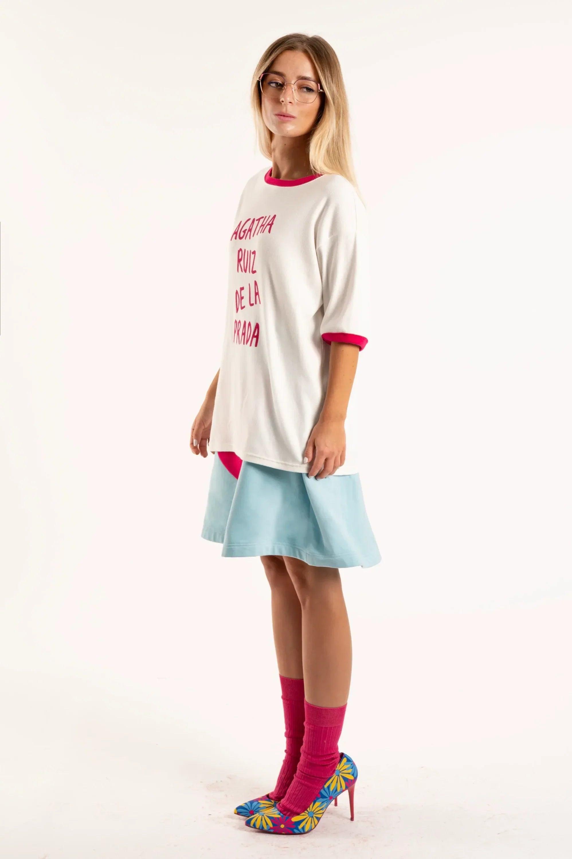Camiseta blanca con borde fucsia en cuello y mangas, letras fucsias en el frente.