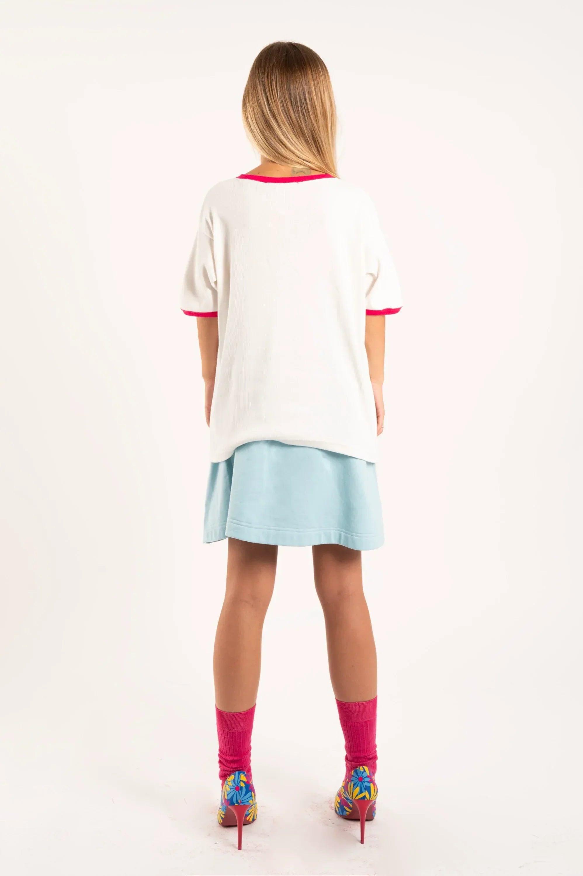 Camiseta blanca con ribete fucsia en cuello y dobladillo, vista trasera.
