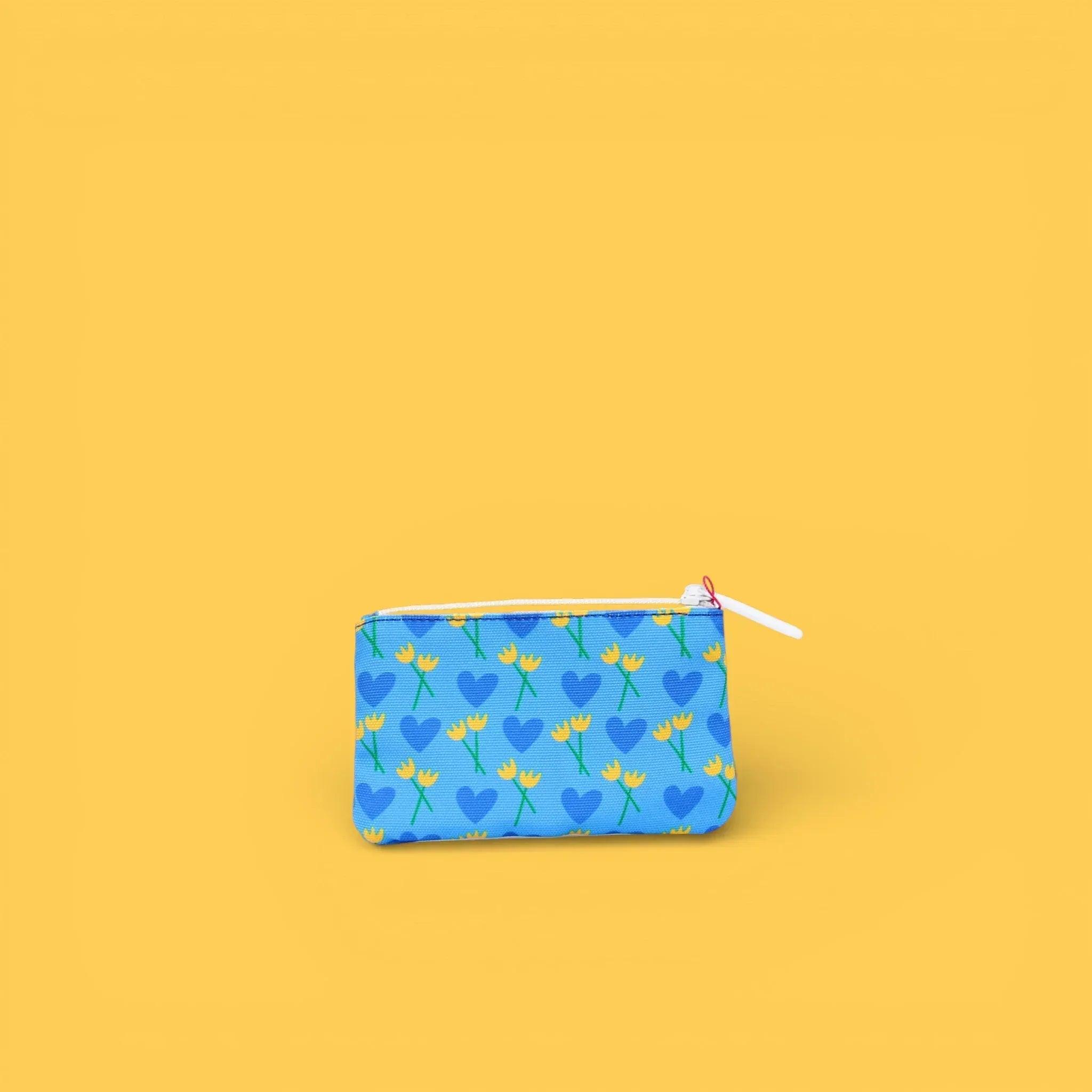 Monedero estampado con cremallera azul y flores amarillas y corazones verdes, vista frontal.