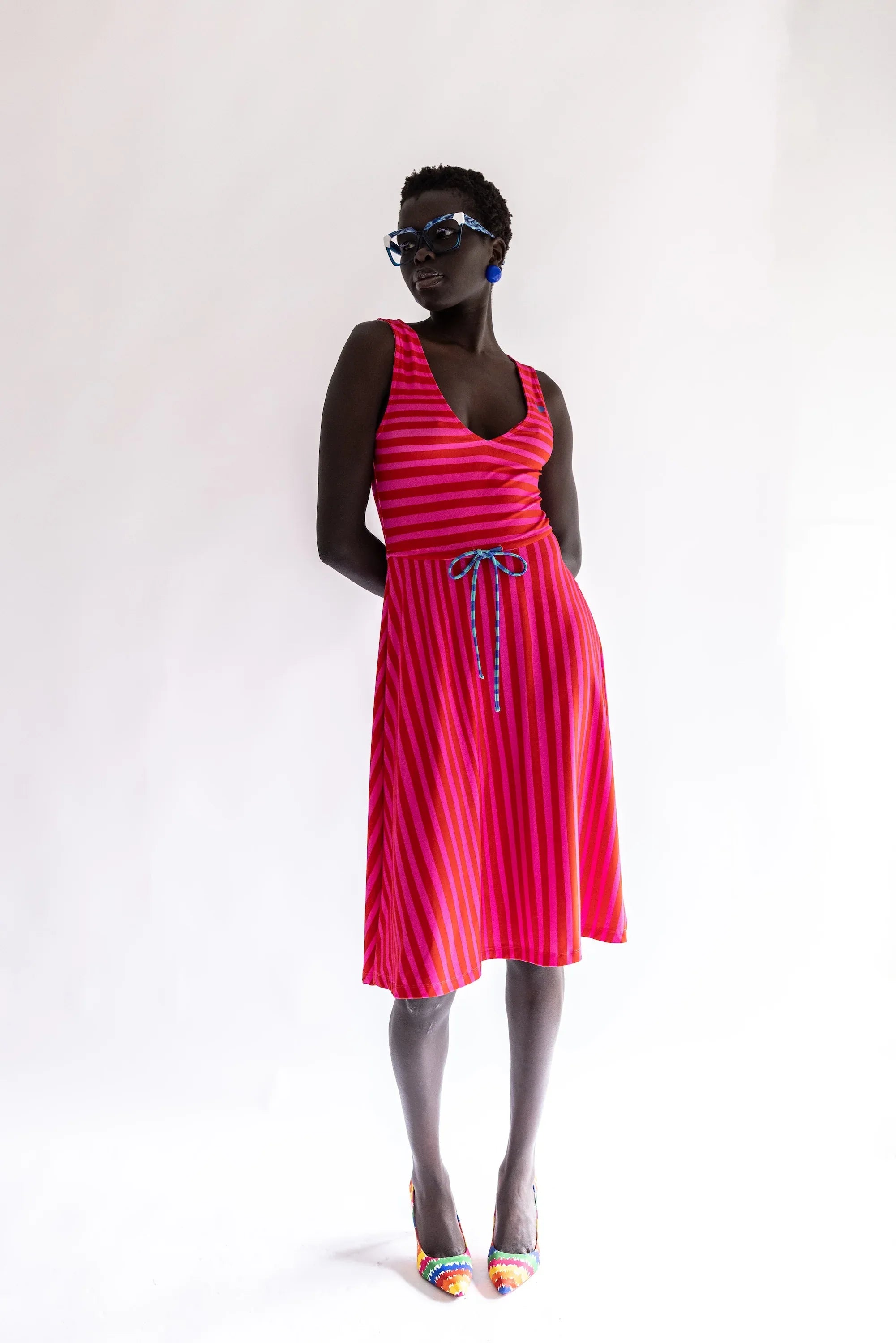 Vestido sin mangas rayado fucsia y rojo, falda plisada y lazo en la cintura.