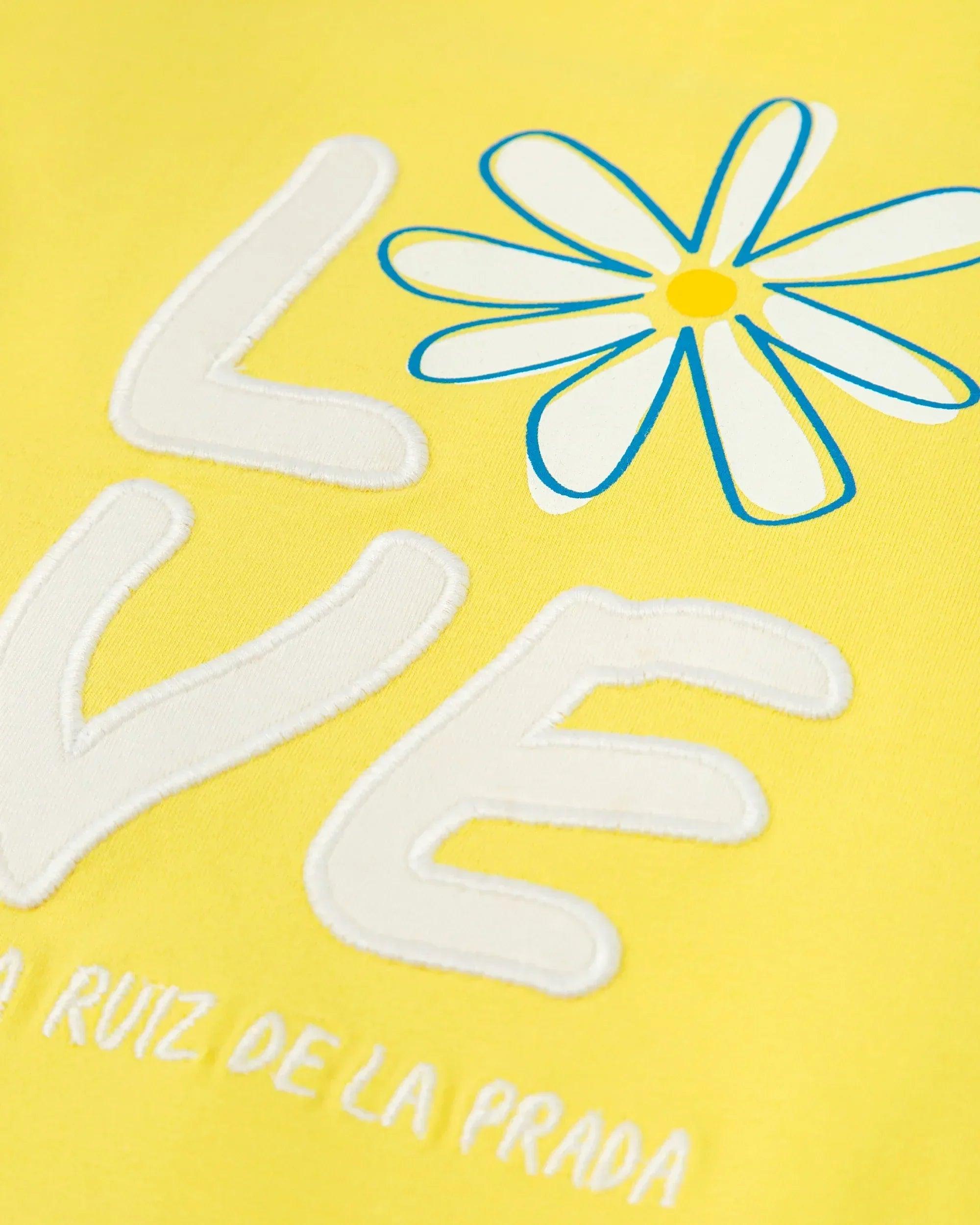Detalle del vestido amarillo: letras LOVE, flor y texto RUIZ DE LA PRADA