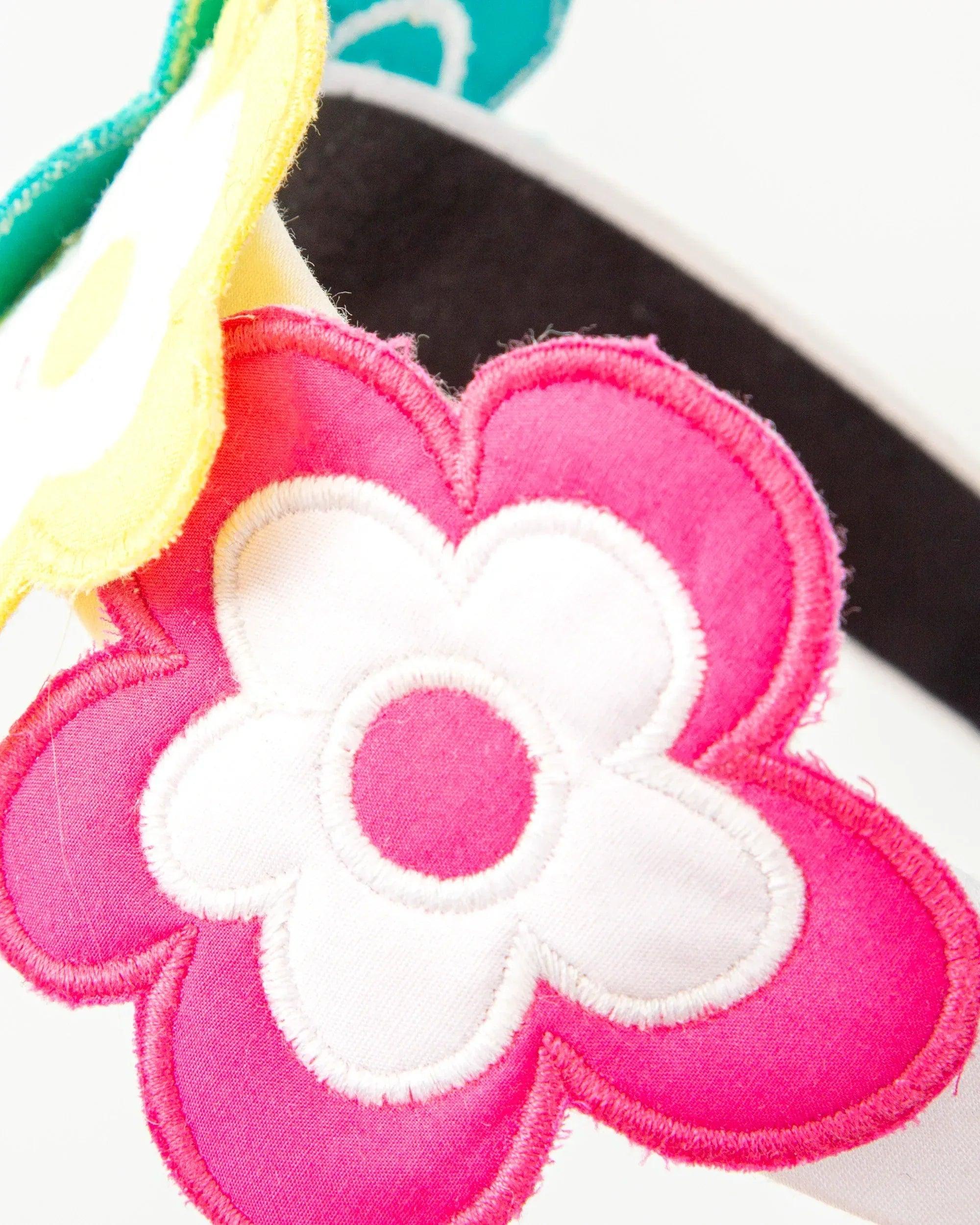Diadema de tela con flor rosa y pétalos blancos sobre base negra